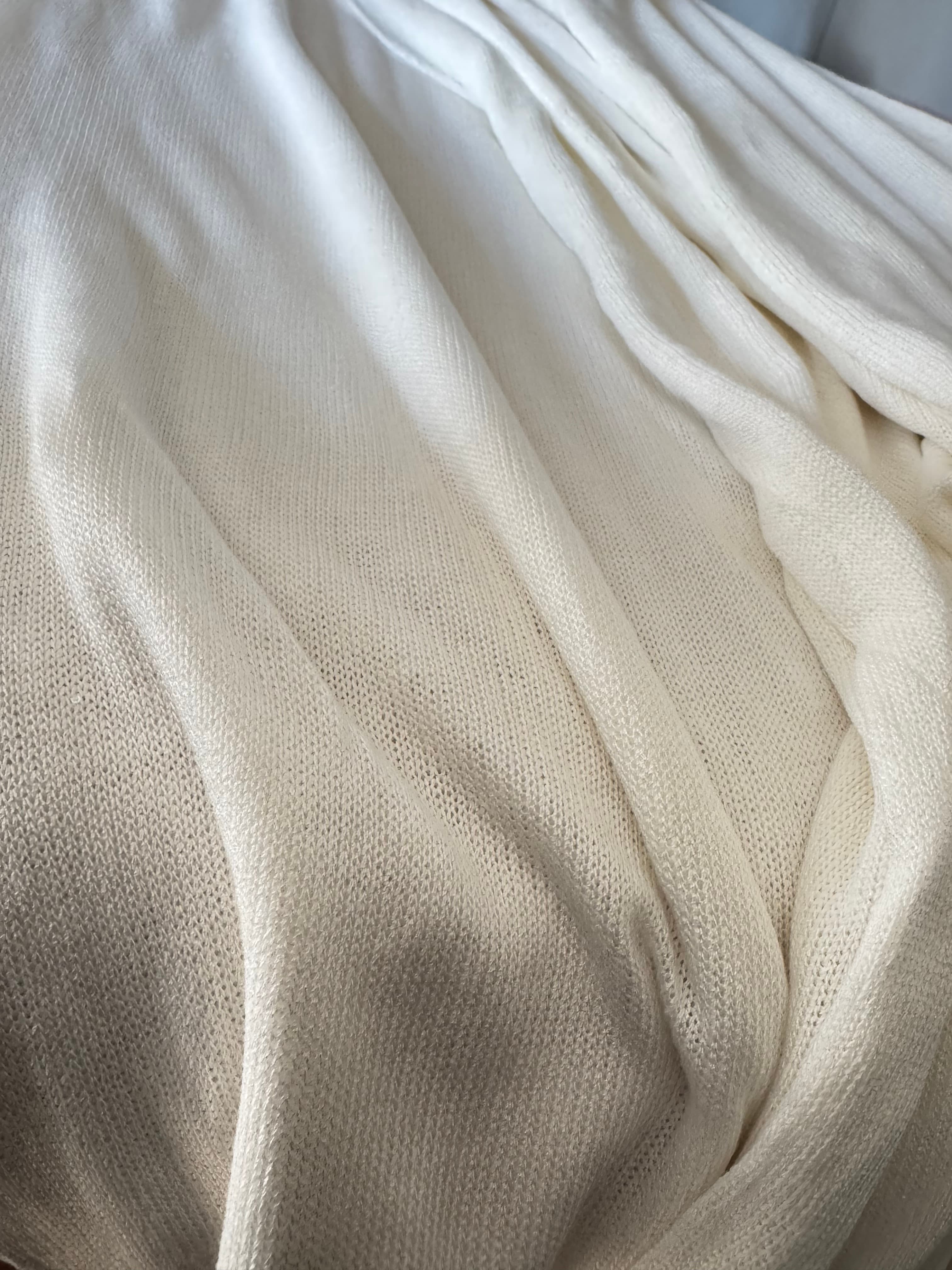 Creamy white, finely knitted fabric cascading in soft, rippling folds with a delicate, translucent texture.