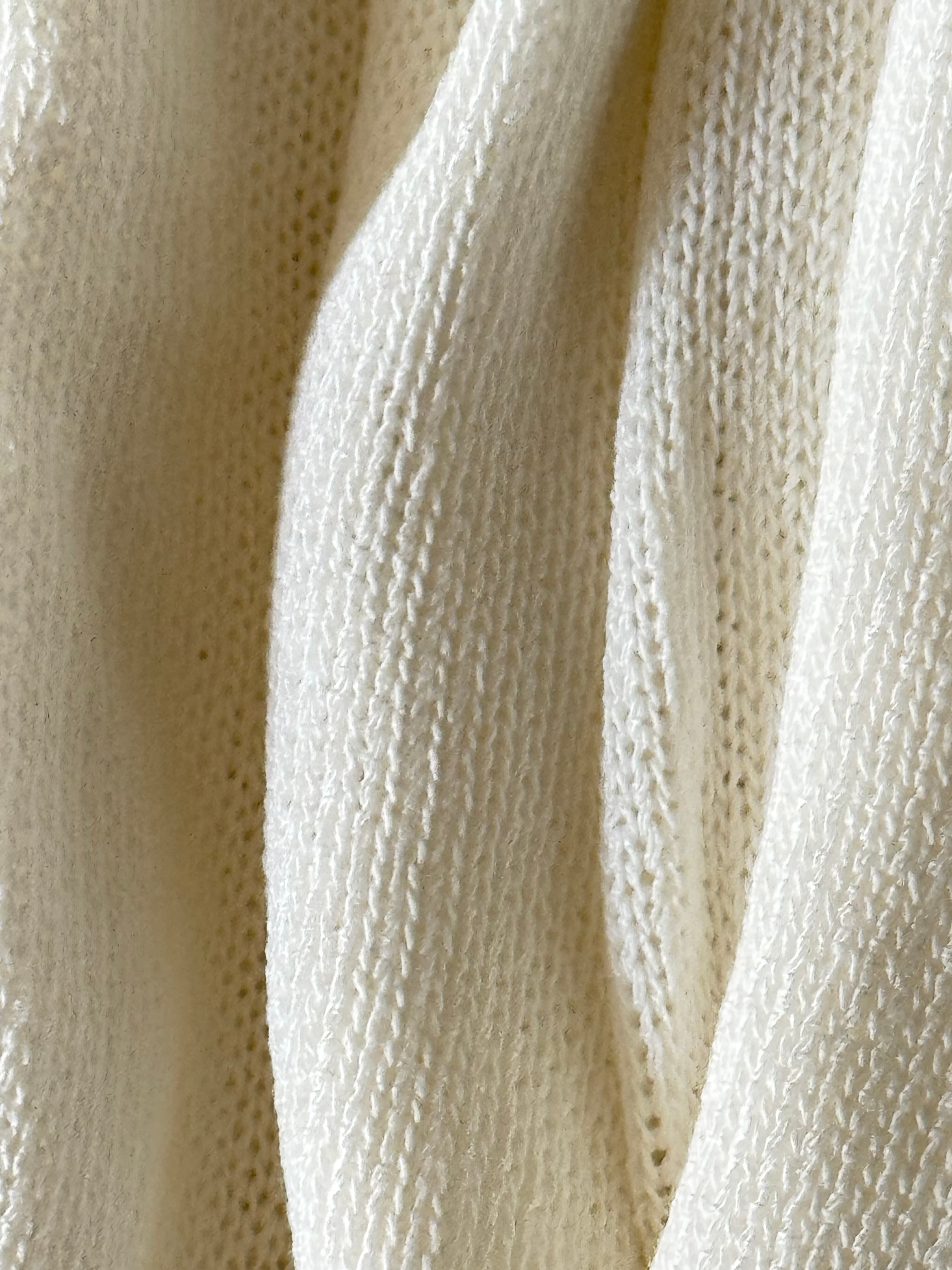 Textured white knit fabric draped in soft vertical folds, highlighting the detailed stitch patterns.