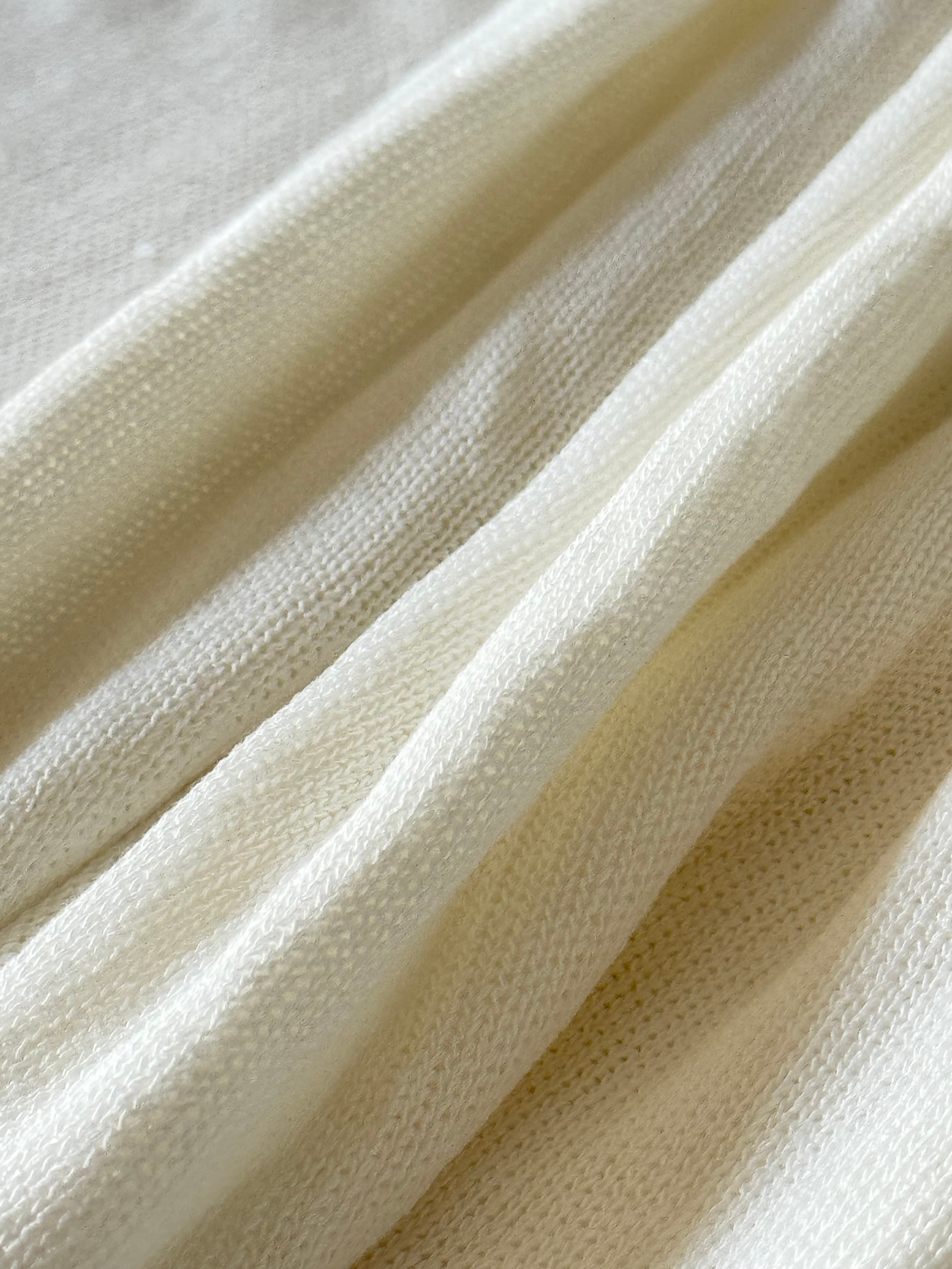 Soft cream-colored knitted fabric draped in elegant folds with a fine, detailed texture.