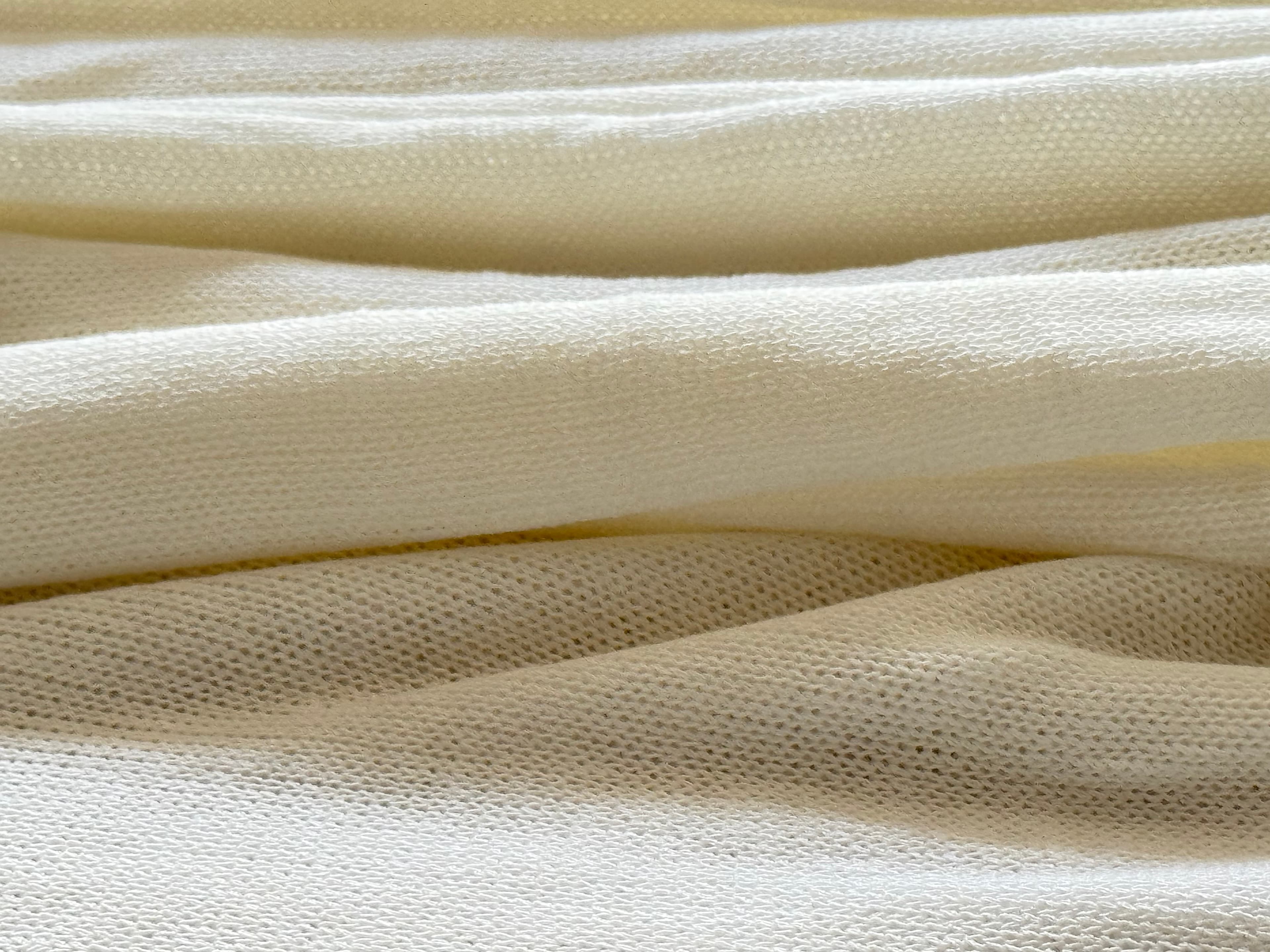 Close-up of cream-colored knitted fabric with soft horizontal folds and a detailed textured weave.