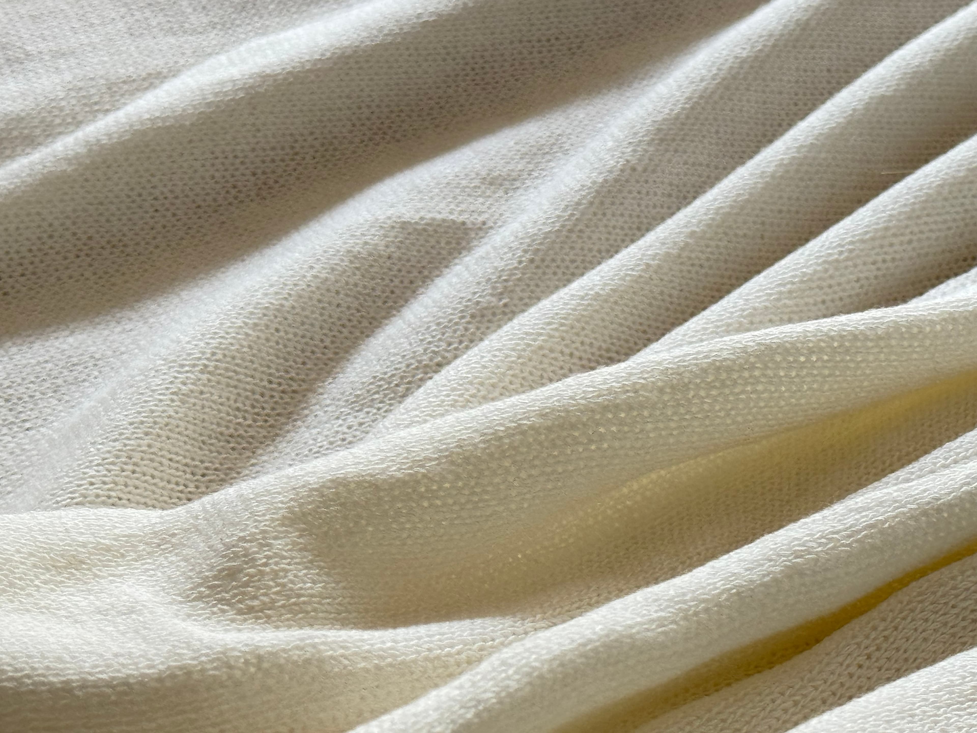 Elegant cream-colored knitted fabric with soft, cascading folds and a fine, cozy texture.